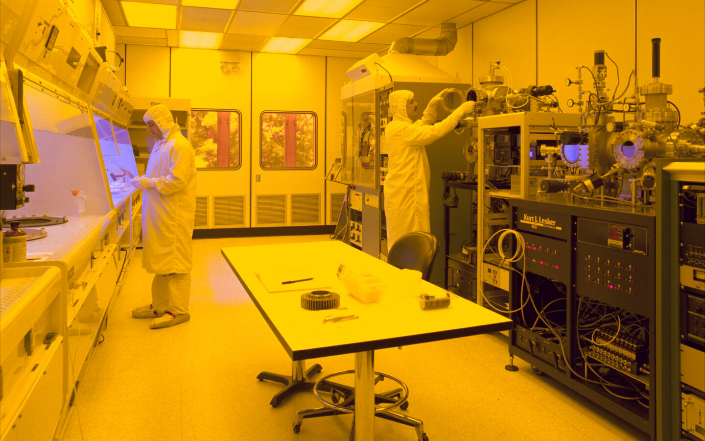 Two people operating equipment in a semiconductor manufacturing cleanroom